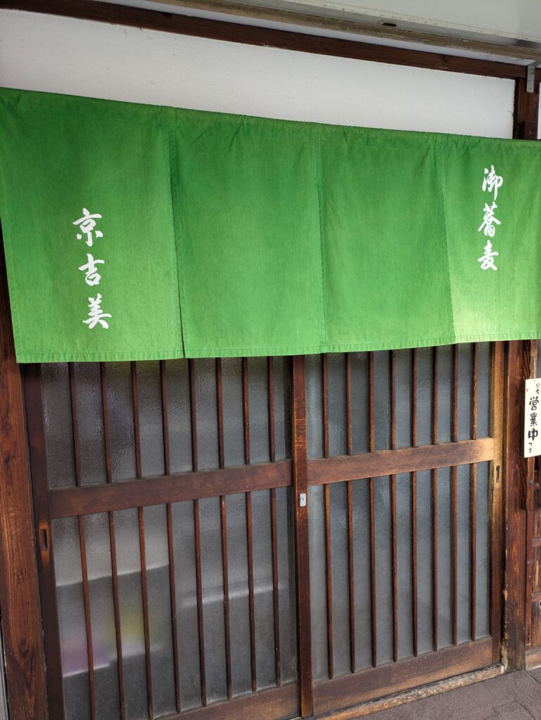 The warm and inviting storefront of Osoba Kyo-Yoshimi, featuring a green noren curtain