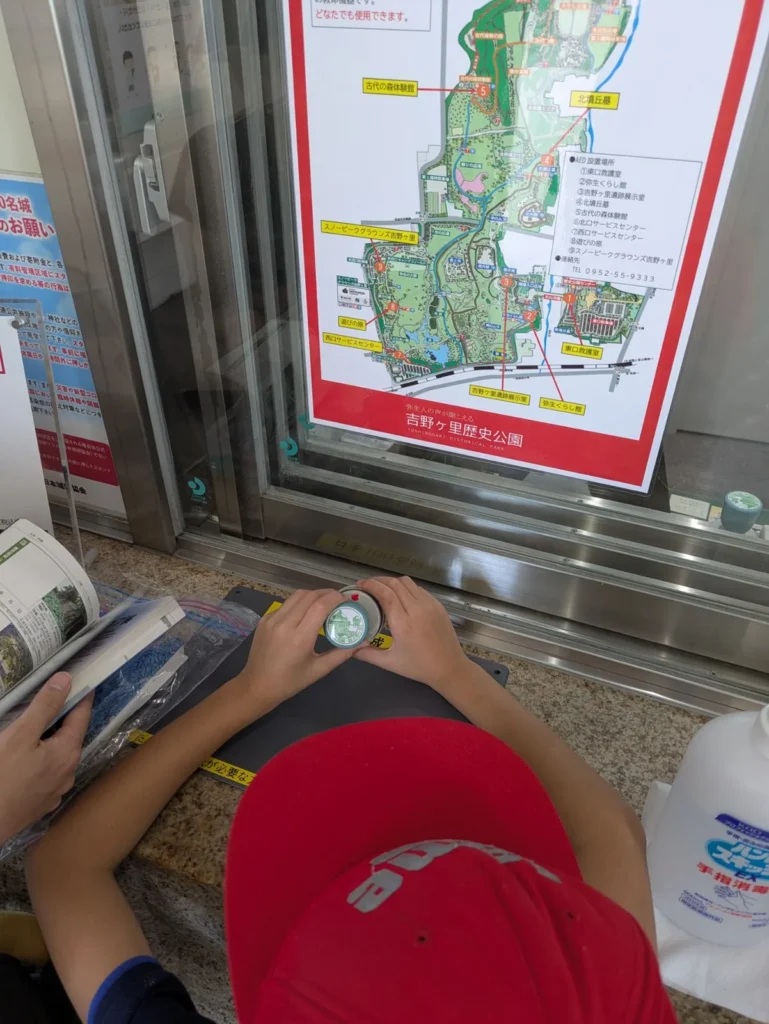 A child stamping the 100 Fine Castles of Japan stamp at the ticket window of Yoshinogari Historical Park